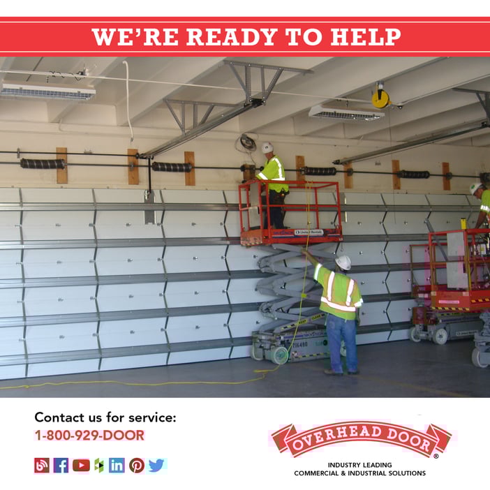 Technicians on scissor lifts repairing a large industrial sectional overhead door for a commercial warehouse.